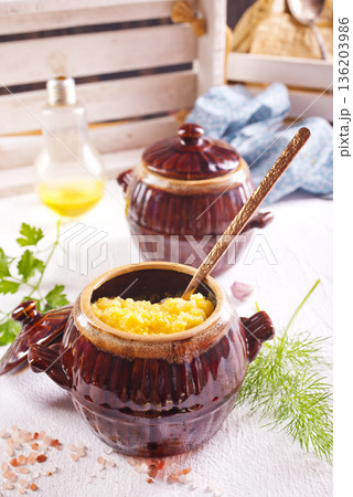 Corn porridge in a clay plate, a clay pot with porridge on a light background 136203986