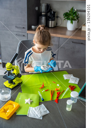 Young girl holding crescent shaped crystal grown at home and carefully examining its surface and structure. Creative STEM experiment combining science learning with artistic crystal growing project. 136204101