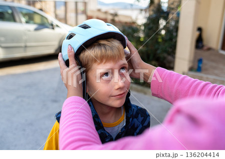 Adult hands adjusting a bicycle helmet on a young boy outdoors, child safety, care and protection before cycling 136204414