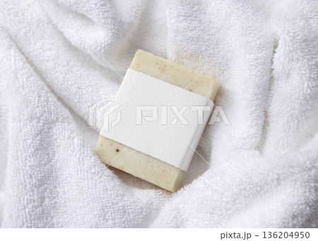 Mockup of beige solid soap bar with blank paper label on white bath towel, personal care packaging 136204950