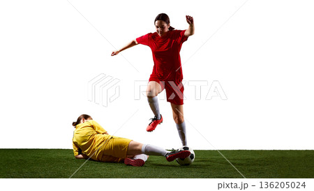 Female soccer player jumping over sliding tackle on field. 136205024