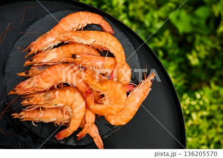 Grilled shrimp on a black grill plate surrounded by green grass in a sunny outdoor setting Grilled shrimp on a black grill plate surrounded by green grass in a sunny outdoor setting 136205570