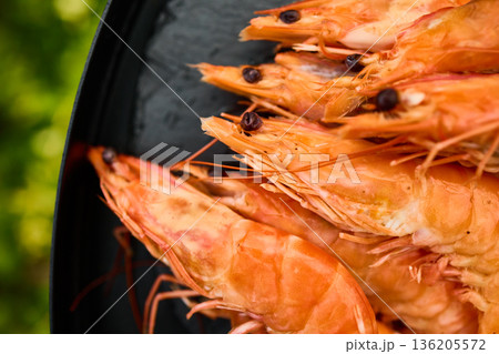 Grilled shrimp on a black grill plate surrounded by green grass in a sunny outdoor setting 136205572