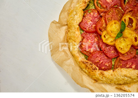 Freshly baked tomato galette on parchment paper served on a rustic wooden table in a cozy kitchen setting 136205574