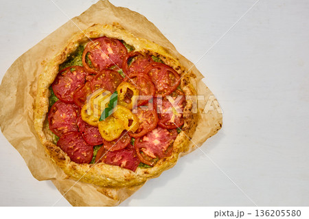 Freshly baked tomato galette on parchment paper served on a rustic wooden table in a cozy kitchen setting 136205580