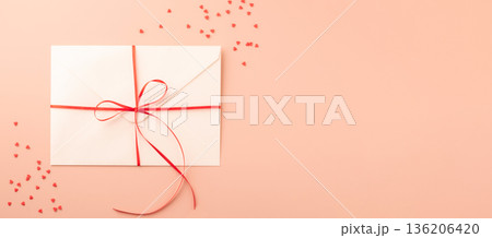 White envelope with red ribbon and sequin heart on pastel background White envelope with red ribbon and sequin heart on pastel background 136206420