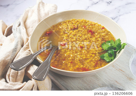 Delicious lentil soup served in a bowl on a rustic surface with garnishes and utensils Delicious lentil soup served in a bowl on a rustic surface with garnishes and utensils 136206606