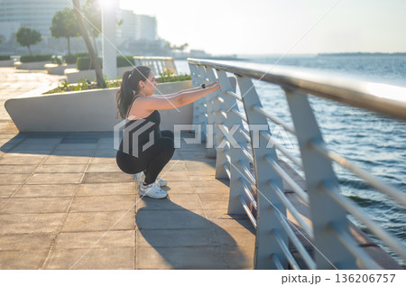 Grounded Prenatal Workout: Woman In A Squat Position By Waterfront Grounded Prenatal Workout: Woman In A Squat Position By Waterfront 136206757