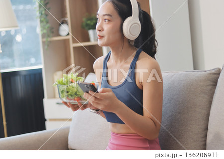 Fit young Asian women in activewear sitting on yoga mat and eating fresh vegetable salad after workout, representing clean eating, fitness lifestyle, wellness routine and health balance. Fit young Asian women in activewear sitting on yoga mat and eating fresh vegetable salad after workout, representing clean eating, fitness lifestyle, wellness routine and health balance. 136206911