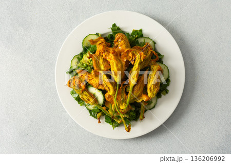 Roasted zucchini flowers sit on a bed of salad made with fresh greens, cucumbers, and broccoli. This dish highlights summer flavors and healthy eating options Roasted zucchini flowers sit on a bed of salad made with fresh greens, cucumbers, and broccoli. This dish highlights summer flavors and healthy eating options 136206992