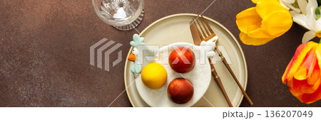 A beautifully arranged Easter table setting showcases a yellow napkin wrapped around a red apple, surrounded by vibrant flowers and a festive bunny decoration, banner A beautifully arranged Easter table setting showcases a yellow napkin wrapped around a red apple, surrounded by vibrant flowers and a festive bunny decoration, banner 136207049