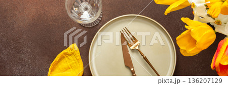 A beautifully arranged spring table setting features a light plate, gold-tone utensils, and vibrant flowers. The yellow napkin adds a pop of color, creating a joyful atmosphere for dining, banner A beautifully arranged spring table setting features a light plate, gold-tone utensils, and vibrant flowers. The yellow napkin adds a pop of color, creating a joyful atmosphere for dining, banner 136207129