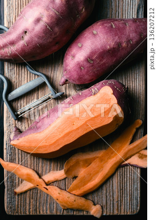 Sweet potatoes with vegetable peeler on wooden cutting board 136207212