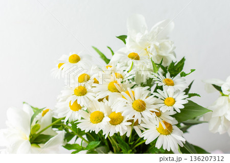 A bouquet featuring bright white daisies with yellow centers is arranged neatly. Green leaves add freshness, creating a cheerful and inviting display suitable for various occasions A bouquet featuring bright white daisies with yellow centers is arranged neatly. Green leaves add freshness, creating a cheerful and inviting display suitable for various occasions 136207312