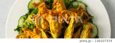 Roasted zucchini flowers sit on a bed of salad made with fresh greens, cucumbers, and broccoli. This dish highlights summer flavors and healthy eating options, banner Roasted zucchini flowers sit on a bed of salad made with fresh greens, cucumbers, and broccoli. This dish highlights summer flavors and healthy eating options, banner 136207354