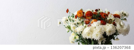 A white pitcher filled with orange and white flowers sits on a light surface. This setup can be used for home decoration or floral arrangement inspiration, banner 136207368