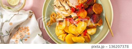 Baked potato is served with chicken breast and roasted carrots, peppers, and beets on a plate. A light meal is arranged on a simple table setting, banner Baked potato is served with chicken breast and roasted carrots, peppers, and beets on a plate. A light meal is arranged on a simple table setting, banner 136207378