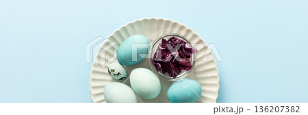 A plate holds several blue-painted Easter eggs and a couple of small patterned eggs, creating a festive atmosphere for the holiday celebration, small bowl of red cabbage, how to dye eggs blue, banner A plate holds several blue-painted Easter eggs and a couple of small patterned eggs, creating a festive atmosphere for the holiday celebration, small bowl of red cabbage, how to dye eggs blue, banner 136207382
