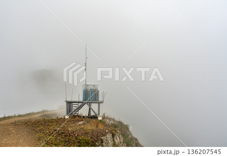 Industrial gas cylinders and technical equipment for anti avalanche installation on mountain ridge in heavy fog copy space 136207545