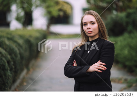 Confident Young Woman Standing with Crossed Arms in Park Wearing Black Jacket Natural Light Shallow Depth of Field and Soft Green Background Confident Young Woman Standing with Crossed Arms in Park Wearing Black Jacket Natural Light Shallow Depth of Field and Soft Green Background 136208537