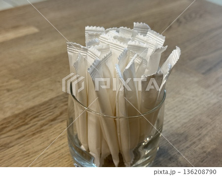 Sugar packets arranged in clear glass on wooden table, perfect for cafe setting or background Sugar packets arranged in clear glass on wooden table, perfect for cafe setting or background 136208790