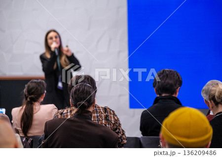 Speaker presenting to audience in conference setting with blue backdrop and attentive attendees Speaker presenting to audience in conference setting with blue backdrop and attentive attendees 136209486
