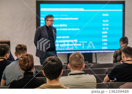 Professional conference presentation with speaker addressing audience in front of blue screen during lecture Professional conference presentation with speaker addressing audience in front of blue screen during lecture 136209489