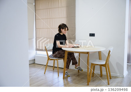 Woman reading book at table in modern kitchen Woman reading book at table in modern kitchen 136209498