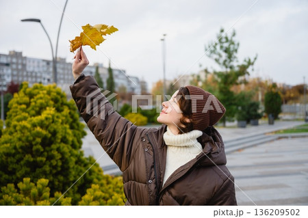 Woman holding autumn leaf in city park 136209502