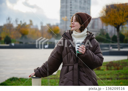 Woman holding takeaway coffee during autumn city walk Woman holding takeaway coffee during autumn city walk 136209516