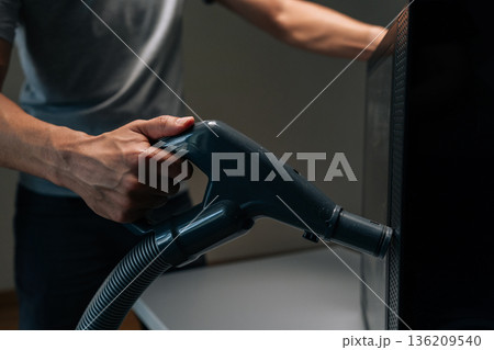 Close-up hands of unrecognizable technician male using vacuum cleaner to remove dust and debris from ventilation holes of computer case, performing important maintenance to prevent overheating. 136209540