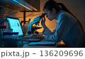 女性がノートPCのグラフを見ながら顕微鏡解析を同時に進める研究風景 136209696