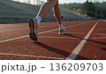 女子高校生が陸上部の練習でトラックを駆け、白線と影が弧を描く放課後 136209703