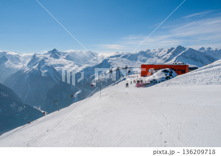 People enjoy skiing and snowboarding in Bad Gastein. The sun shines on the snow-covered slopes. Ski lifts take riders to the top of the mountain. Beautiful mountains surround the area. 136209718