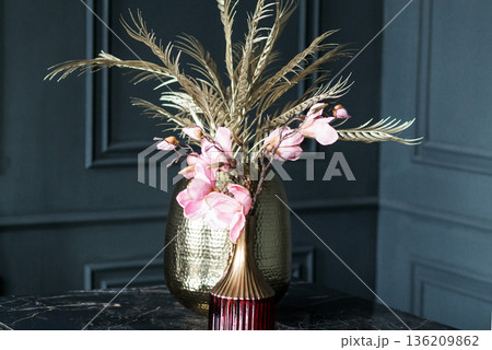 Elegant arrangement of pink flowers and golden leaves in a stylish vase on a dark marble table, enhancing the modern interior decor with a touch of sophistication Elegant arrangement of pink flowers and golden leaves in a stylish vase on a dark marble table, enhancing the modern interior decor with a touch of sophistication 136209862