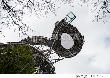 A wooden structure rises against the sky. People stand on the observation deck at the top. Cloudy weather surrounds the area and trees are viewed below. A wooden structure rises against the sky. People stand on the observation deck at the top. Cloudy weather surrounds the area and trees are viewed below. 136210228