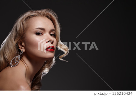 Confident Lady With Luminous Makeup. Stylish Fairhaired Woman With Shimmering Earrings. Sophisticated Caucasian Female Featuring Dazzling Jewelry And Flawless Dewy Skin In Studio Setting 136210424
