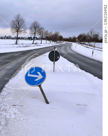A bent road sign "Turn right" on the snow-covered shoulder of a country road 136210492