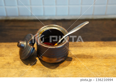 top view Chili paste in a brown ceramic cup Inside is a silver spoon. There is a lid placed on the side of the cup on wooden floor, white ceramic tile background top view Chili paste in a brown ceramic cup Inside is a silver spoon. There is a lid placed on the side of the cup on wooden floor, white ceramic tile background 136210994