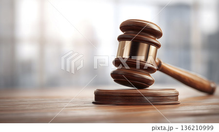 Wooden gavel is on a wooden surface. The gavel is brown and has a gold stripe Wooden gavel is on a wooden surface. The gavel is brown and has a gold stripe 136210999