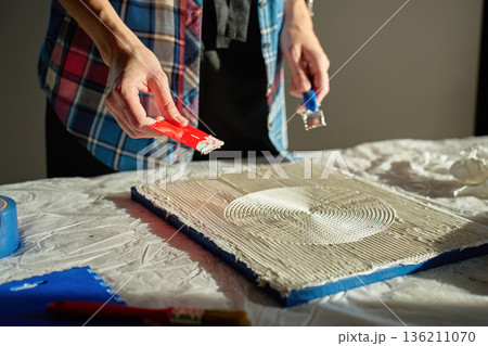 Hands holding tools above board covered with thick paste shaped into circular textured pattern Hands holding tools above board covered with thick paste shaped into circular textured pattern 136211070
