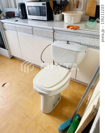 White toilet positioned in a kitchen setting, surrounded by household items, showcasing an unusual interior design choice and practical home environment 136211283