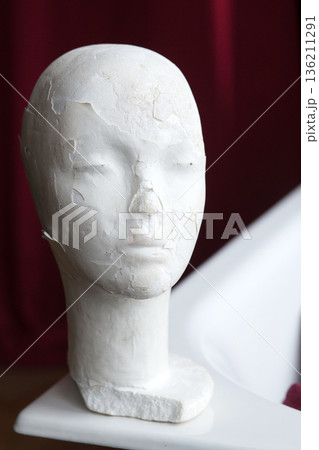White plaster mannequin head with cracked surface texture, positioned on a white surface, showcasing artistic details and unique design elements in a creative environment White plaster mannequin head with cracked surface texture, positioned on a white surface, showcasing artistic details and unique design elements in a creative environment 136211291