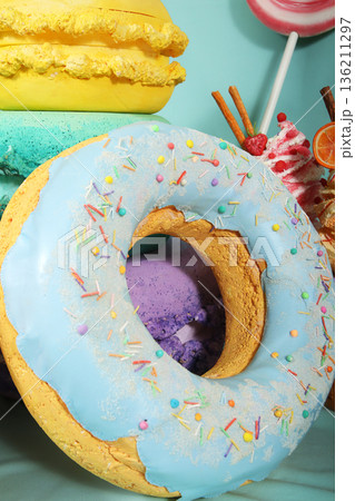 Colorful artificial sweets including a large donut with blue icing and sprinkles, set against a vibrant turquoise background, showcasing a playful dessert concept with copy space 136211297