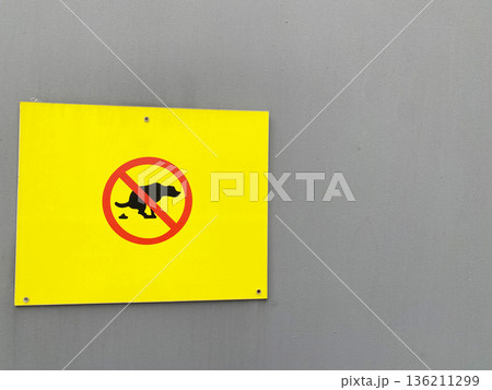 Bright yellow sign on a gray wall indicating prohibition of dog walking and animal waste, featuring a graphic of a dog and a crossed-out symbol, emphasizing cleanliness and regulations 136211299