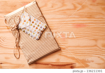 Gift-wrapped package with decorative envelope on a rustic wooden background, showcasing a warm and inviting atmosphere perfect for celebrations and special occasions 136211301