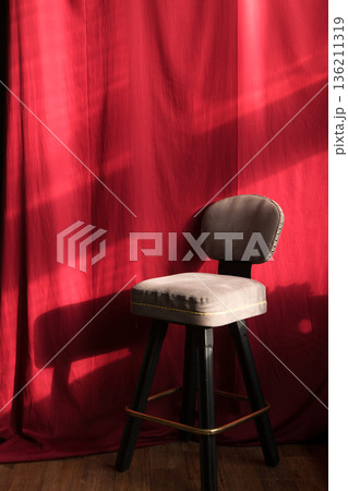 Elegant gray upholstered bar stool positioned against a rich red backdrop, showcasing soft textures and dramatic lighting, creating a warm and inviting atmosphere 136211319