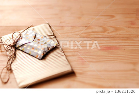 Gift-wrapped package with decorative envelope tied with twine, resting on a wooden surface, creating a warm and inviting atmosphere for special occasions 136211320