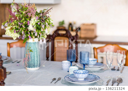 Elegant dining table set with blue and white porcelain dishes, glassware, and a vibrant floral centerpiece, creating a warm and inviting atmosphere for gatherings Elegant dining table set with blue and white porcelain dishes, glassware, and a vibrant floral centerpiece, creating a warm and inviting atmosphere for gatherings 136211324
