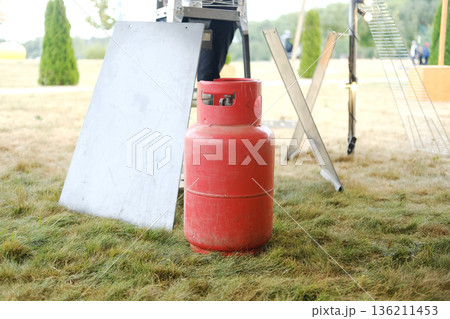 Red propane gas cylinder positioned on grass beside metal sheet and tools, illustrating preparation for heat gun use in outdoor setting with copy space Red propane gas cylinder positioned on grass beside metal sheet and tools, illustrating preparation for heat gun use in outdoor setting with copy space 136211453
